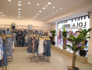 Vista del interior de la tienda de ropa Lola Ruiz con percheros de prendas de moda femenina en tonos azules y blancos.